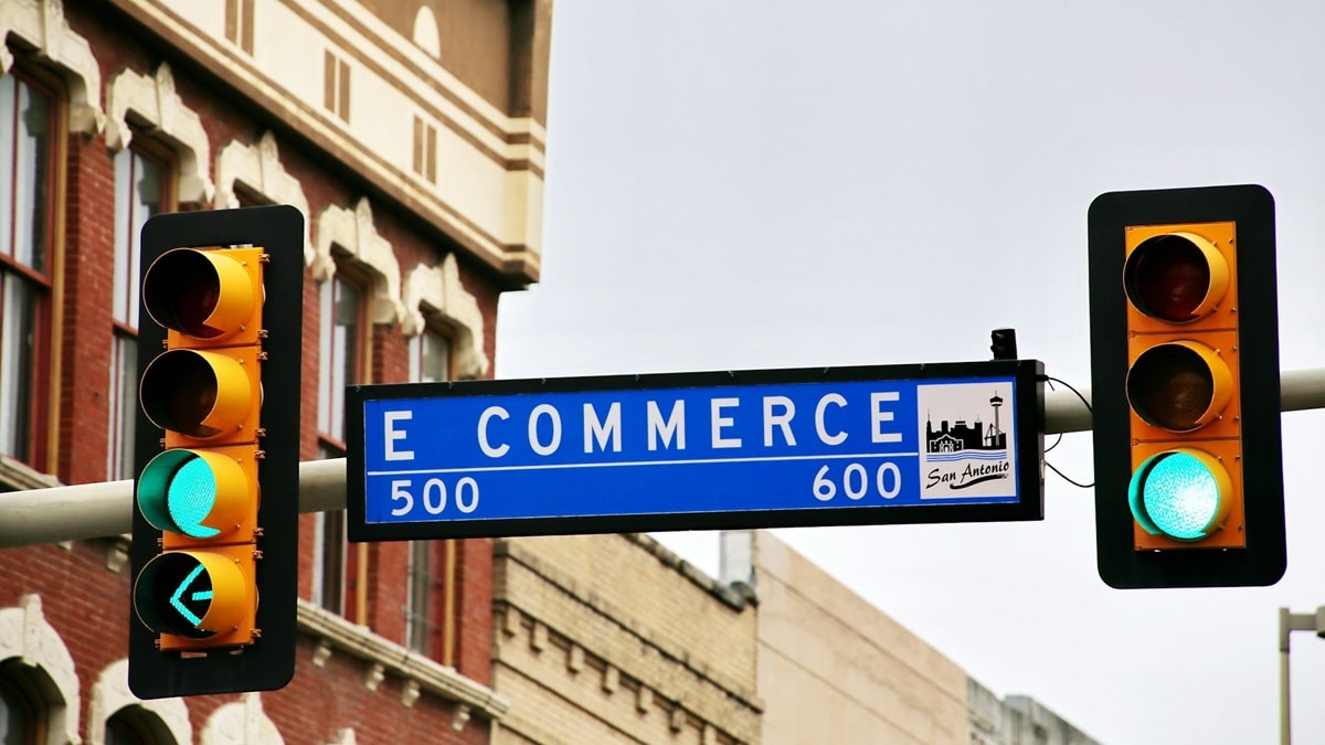 A street sign between two traffic lights that says E-COMMERCE